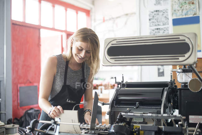Young woman working with traditional letterpress print machine in workshop — Stock Photo