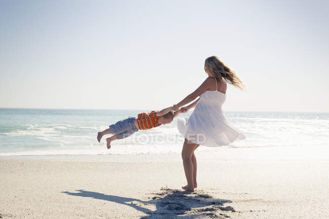 Mid adult mother swinging little son by hands on beach, Cape Town, Western Cape, South Africa — Stock Photo