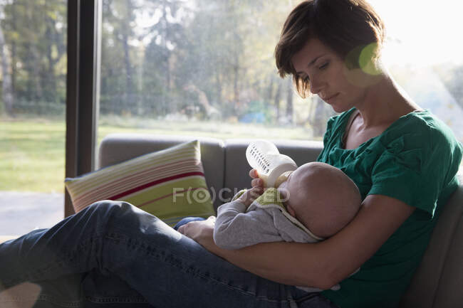 Mother feeding bottle to baby boy on sofa — Stock Photo