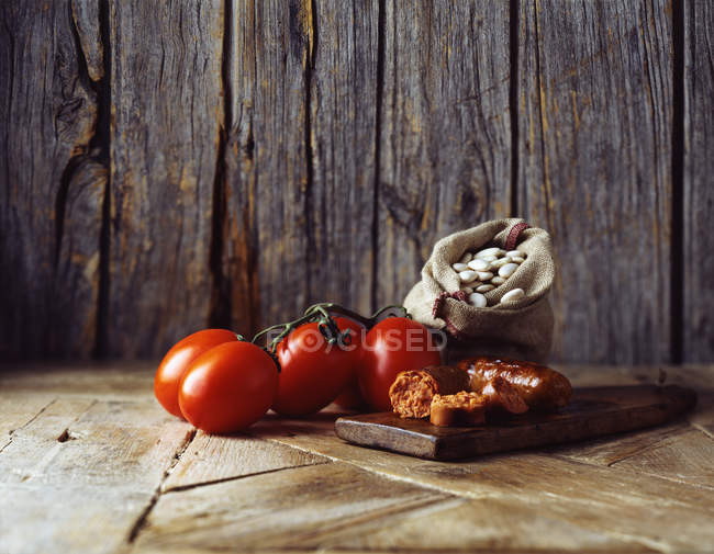 Tomaten, Chorizo und Butterbohnen im Kleesack auf einem Holzschneidebrett — Stockfoto