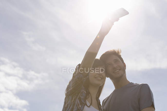Couple adolescent prenant selfie sur téléphone mobile sous un ciel ensoleillé lumineux — Photo de stock