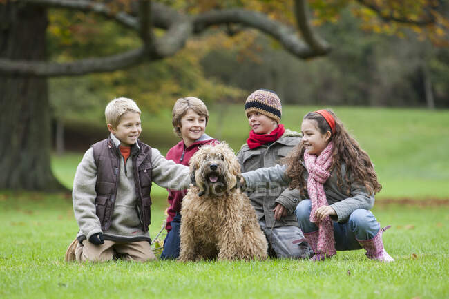 Quattro bambini nel parco, accovacciati, accarezzando il cane — Foto stock