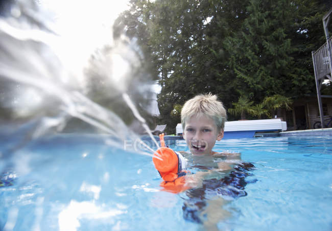 Menino na piscina esguichando pistola de água — Fotografia de Stock