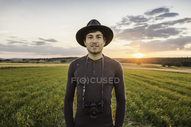 Porträt eines Mannes, der mit Slr-Kamera um den Hals auf dem Feld steht — Stockfoto