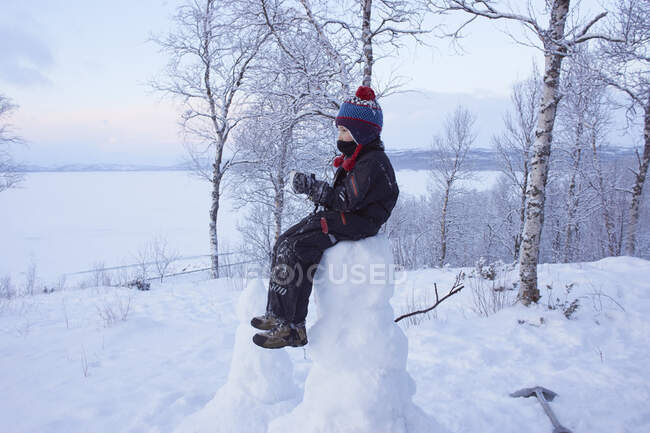 Niño sentado en la parte superior del hombre de la nieve, Hemavan, Suecia - foto de stock
