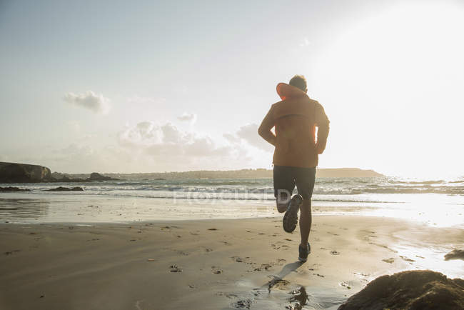 Зрелый человек бежит по песку вдоль береговой линии — стоковое фото