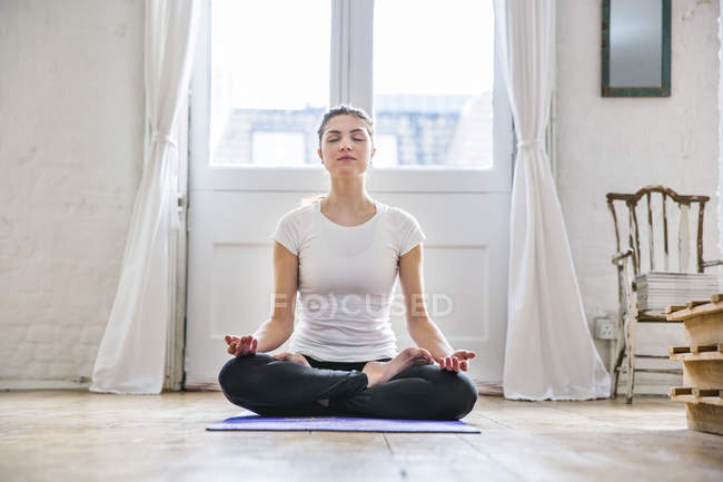 Jovem mulher praticando ioga posição de lótus no apartamento — Fotografia de Stock
