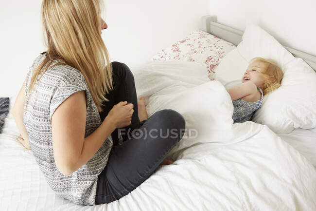 Mid adult woman sitting on bed with toddler daughter at bedtime — Stock Photo