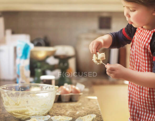 Niño sosteniendo cuchara con mezcla de pastel - foto de stock
