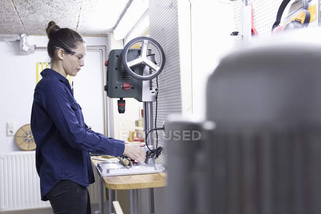 Young female carpenter drilling timber in workshop — Stock Photo