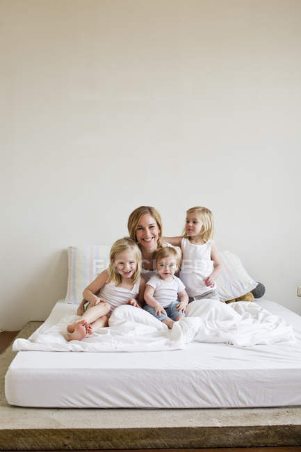 Porträt einer erwachsenen Frau mit drei Töchtern im Bett — Stockfoto