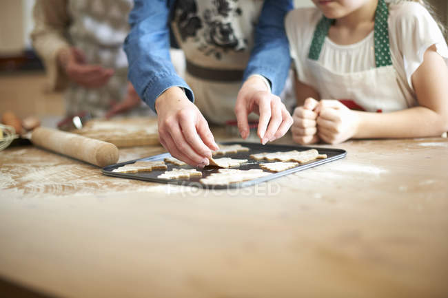 Tiro cortado de mulher sênior e netas colocando biscoitos de árvore de Natal na bandeja de cozimento — Fotografia de Stock