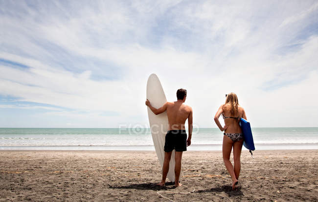 Giovane coppia in piedi sulla spiaggia in possesso di tavola da surf e boogie board — Foto stock