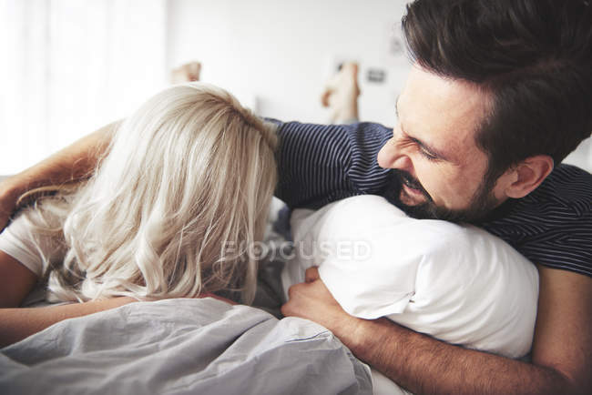 Пара лежить на ліжку, чоловік лоскоче жінку — стокове фото