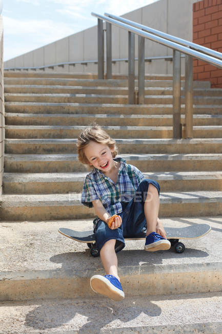 Мальчик сидит на скейтборде на ступеньках — стоковое фото