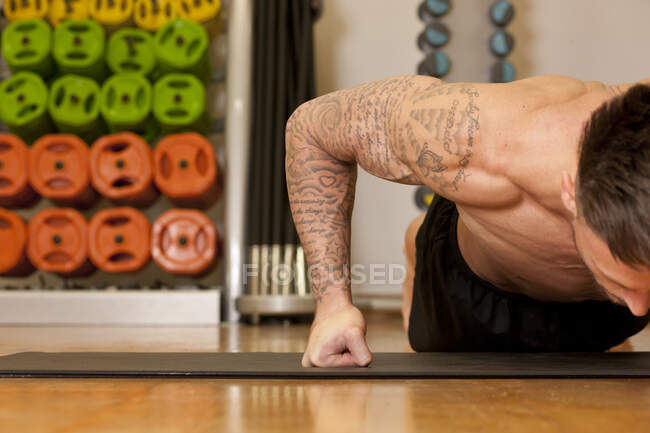 Татуйований чоловік вправляється на йога килимок у спортзалі — стокове фото