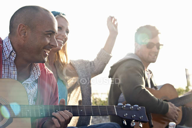 Трое друзей играют на акустических гитарах на пляже Борнмута, Дорсет, Великобритания — стоковое фото