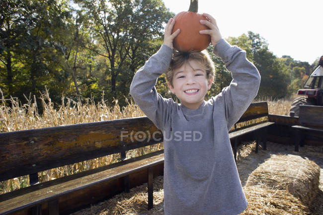 Portrait of cute boy holding up pumpkin on head — Stock Photo
