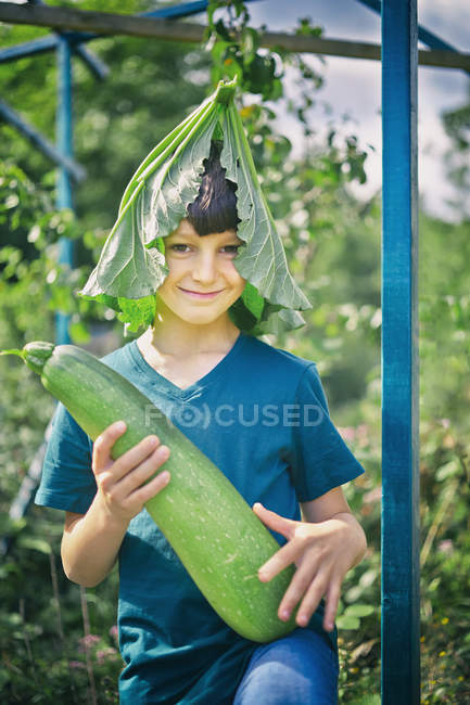 Portrait of boy with leaf hat and marrow on allotment — Stock Photo