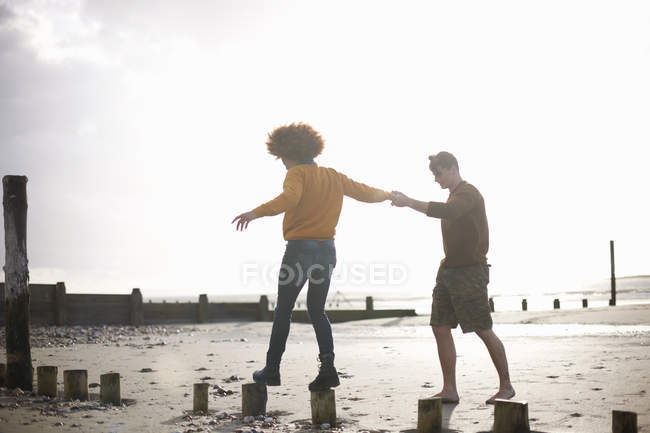Man helping woman balance on wooden stumps on beach — Stock Photo