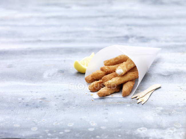 Greaseproof paper cone with lemon sole goujons on steel table — Stock Photo