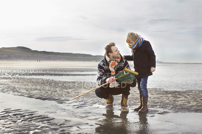 Hombre adulto y su hijo con red de pesca en la playa, Bloemendaal aan Zee, Países Bajos - foto de stock
