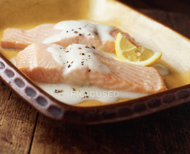 Baked salmon with bechamel sauce and lemon wedge in ceramic baking tin — Stock Photo