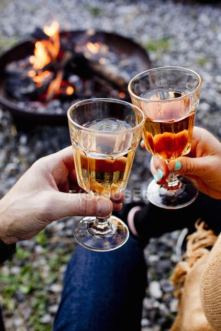 Deux personnes grillent avec des boissons dans des verres à vin près du feu — Photo de stock