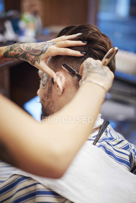 Hairdresser shaving customer's hair with straight razor — Stock Photo