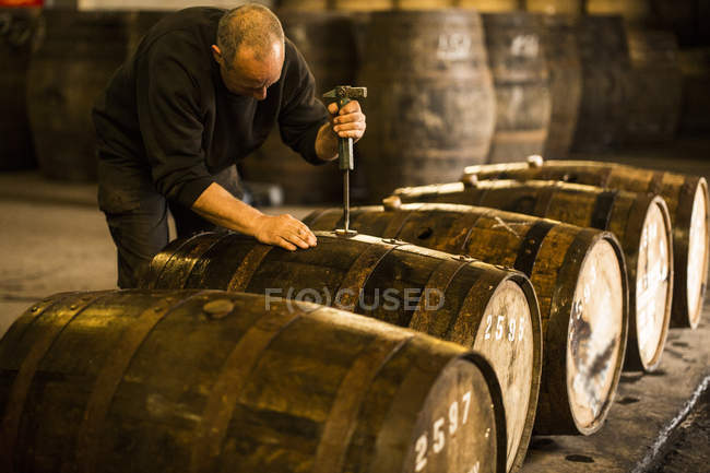 Male worker opening wooden whisky cask in whisky distillery — Stock Photo