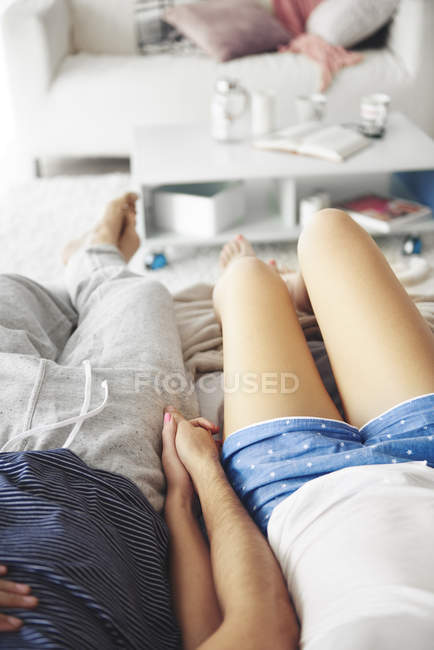 Couple relaxing at home, holding hands, low section — Stock Photo