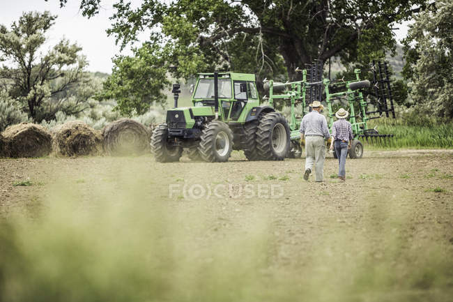 Вид сзади на фермера и мальчика-подростка, идущего по вспаханному полю — стоковое фото