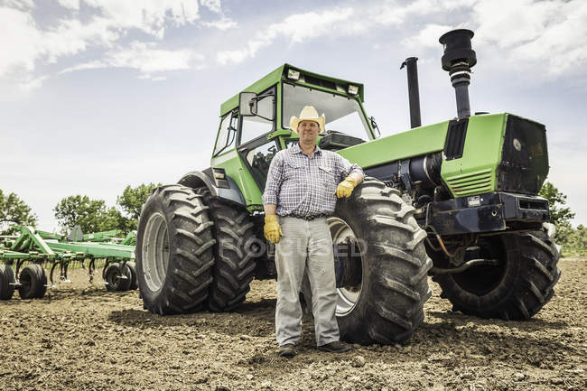 Retrato del agricultor macho apoyado contra el tractor en el campo arado - foto de stock