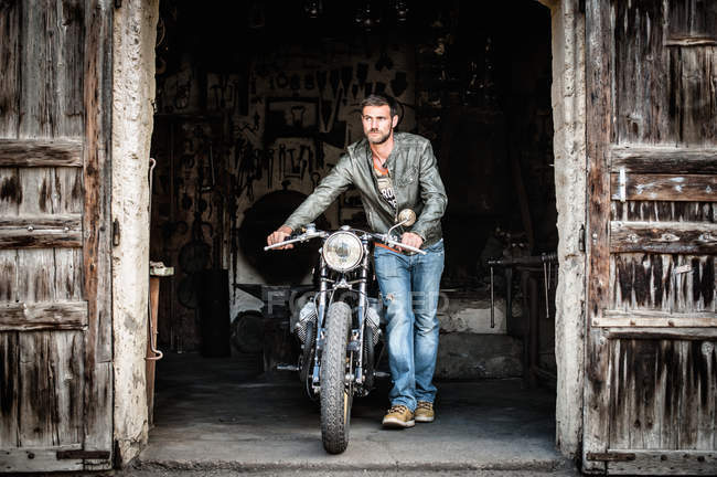 Молодой человек выталкивает мотоцикл из двери сарая — стоковое фото