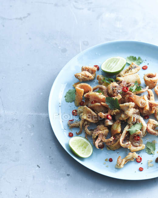 Top view of salt and pepper chilli squid garnished with lemon and coriander on plate — Stock Photo