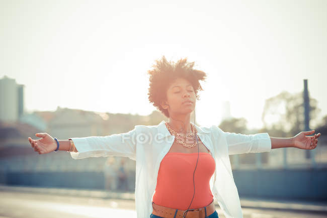 Young woman dancing with arms open to smartphone music in city — Stock Photo