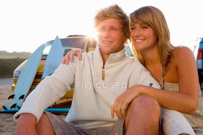 Пара сидить на пляжі посміхається з фургоном — стокове фото