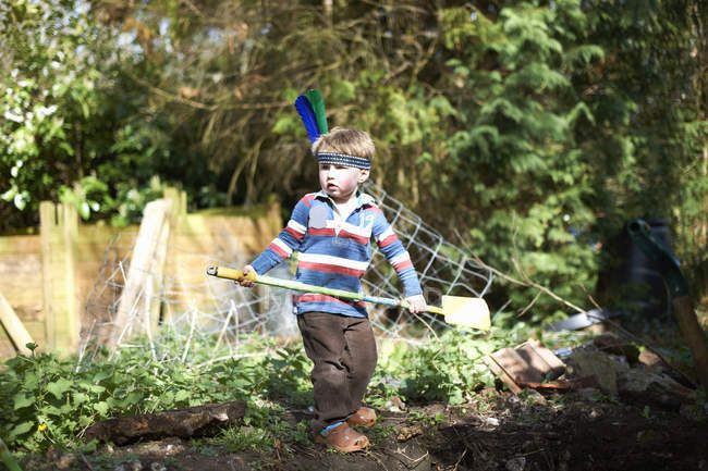 Молодий хлопчик носить пов'язку з пір'ям, тримаючи лопату — стокове фото