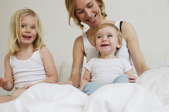 Retrato de mulher adulta média na cama com duas filhas — Fotografia de Stock