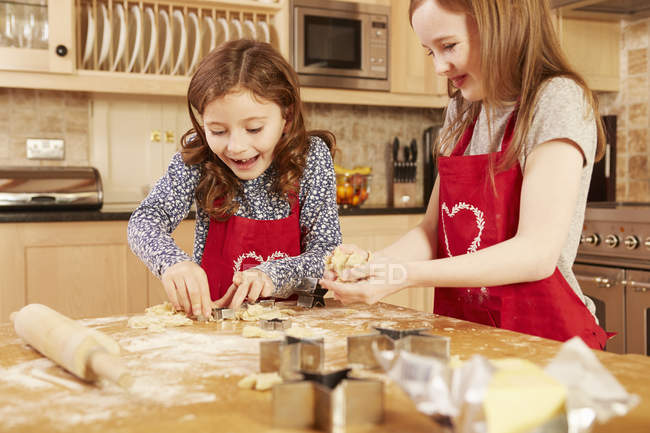 Dos chicas haciendo pastelería de forma estrella en la mesa de la cocina - foto de stock
