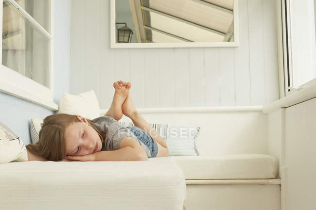 Sullen chica acostada en el asiento del apartamento de vacaciones - foto de stock