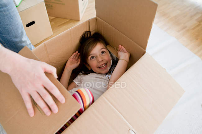 Улыбающаяся девушка играет в картонной коробке — стоковое фото