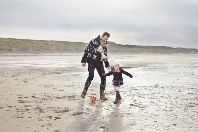 Взрослый мужчина с дочерью, играющей в футбол на пляже, Блумендал-ан-Зи, Нидерланды — стоковое фото