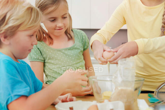 Діти випікають, розбиваючи яйця в миску — стокове фото
