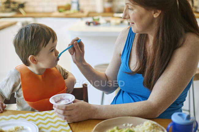 Femme nourrissant bébé fils à table — Photo de stock