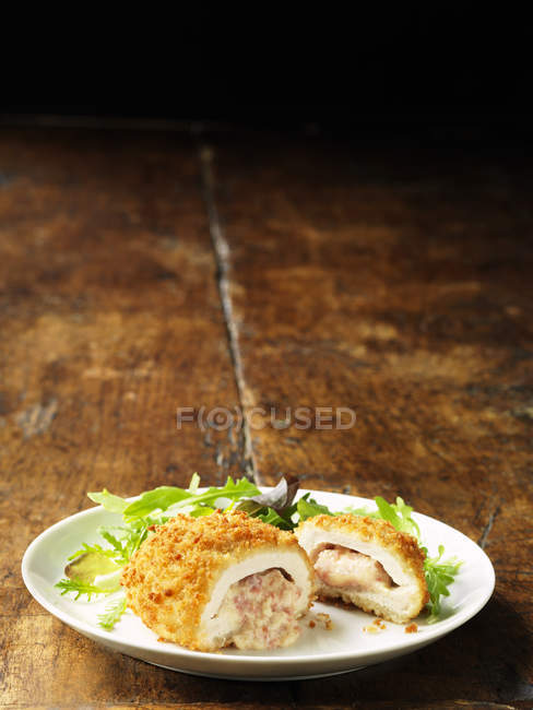 Chicken Kiev with cheese and ham filling on white plate with green salad leaves — Stock Photo
