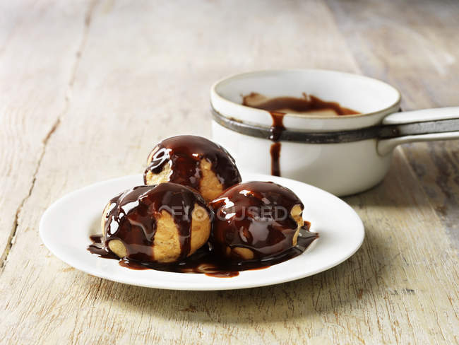 Profiteroles with hot chocolate sauce on white plate — Stock Photo