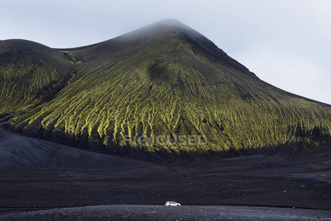 Машина припаркована на черном песке под большим зеленым холмом — стоковое фото