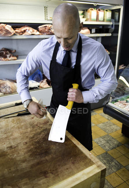 Carnicero limpiando cuchillo de carne en carnicería - foto de stock