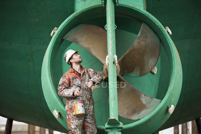 Pintor de barcos macho inspeccionando casco de barco verde en astillero de pintores - foto de stock